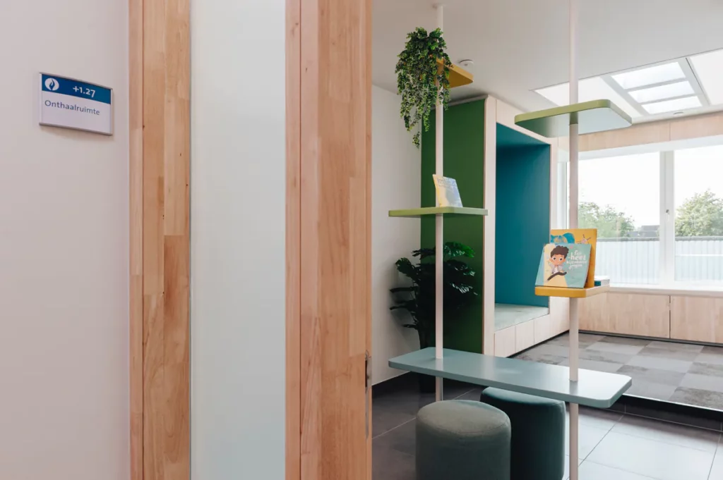 Inkijk in de wachtruimte van de videoverhoorkamer in Eeklo, met houten kastenwand en groenblauwe accenten