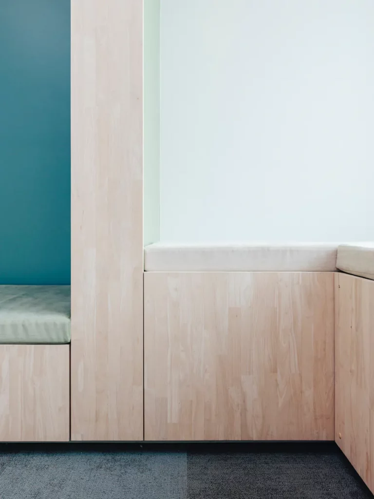 Detail van de houten kastenwand met zitbank en groenblauwe nis in de wachtruimte