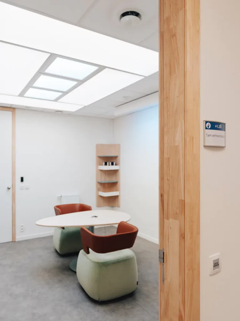 Videoverhoorkamer met verlicht plafondpaneel, ovale tafel en zachte fauteuils